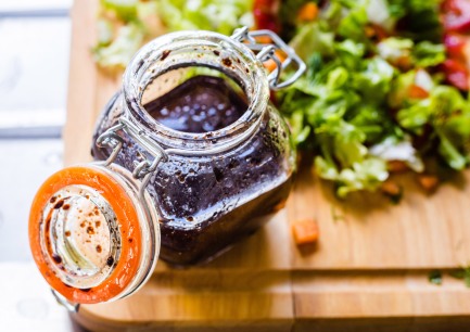 A Glass Bottle with Salad Dressing consisting of Balsamic Vinegar, Olive Oil, Pepper and Salt, Salad on the Background